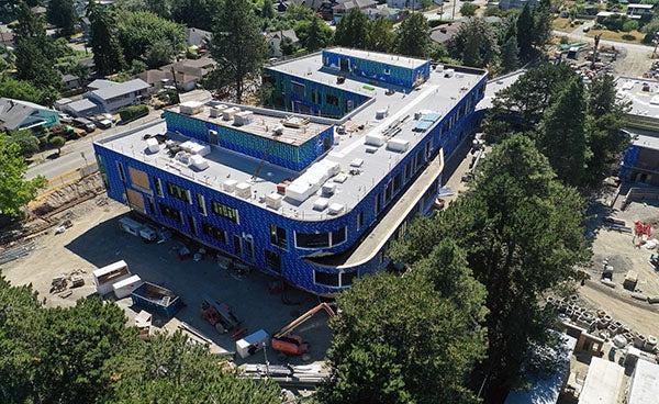 aerial view of a building under construction with a flat gray roof with skylights andblue material on exterior walls