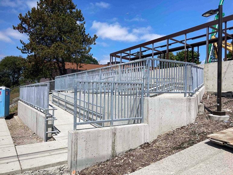 a concrete ramp zig zags on a hill with concrete short walls with metal railings and fence